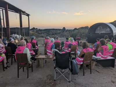 people wearing pink hivis vests watching a discuussion and film screening with the estuary in the backdrop
